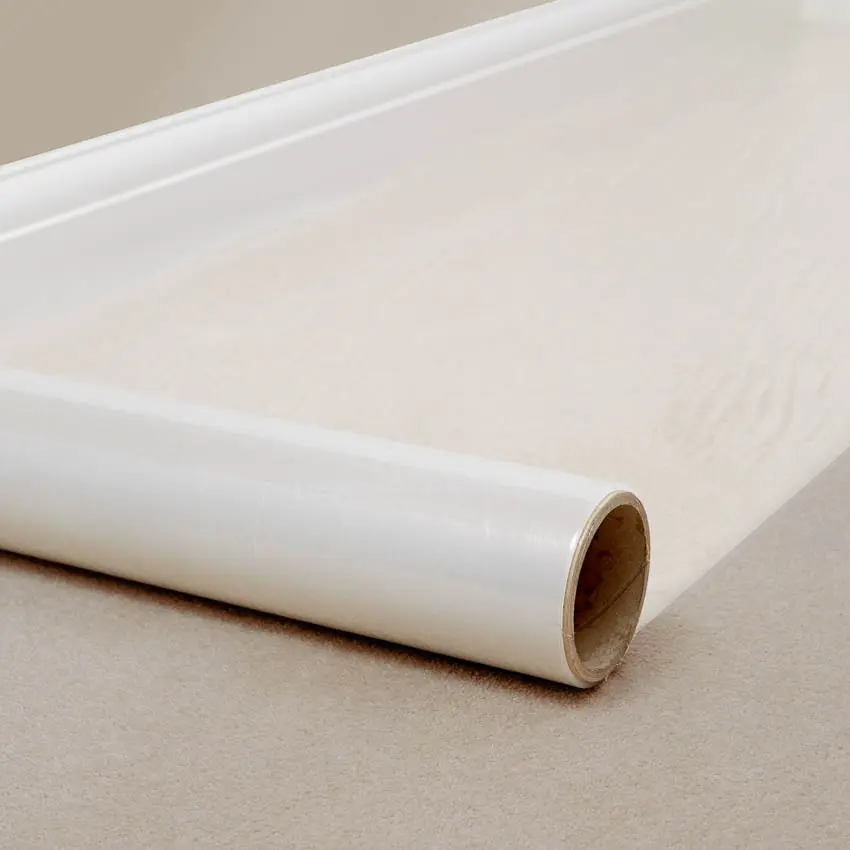 A roll of transparent carpet protector film being rolled out onto a white carpet