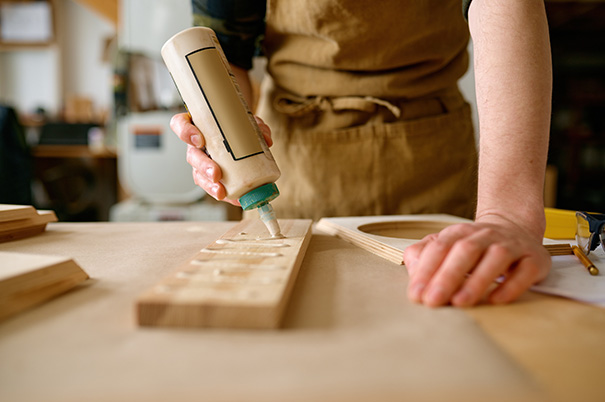 Carpenter standing at a workbench and squeezing a bead of wood glue onto a piece of wood