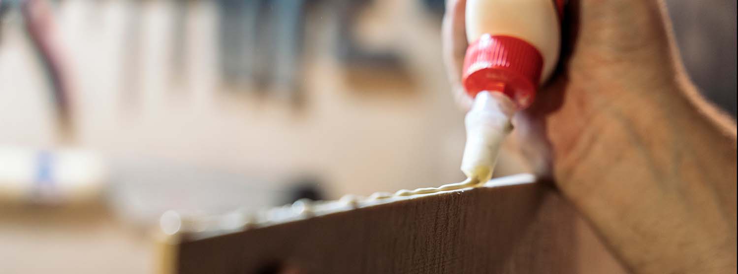 Close up of wood glue being precisely applied from a bottle to a piece of wood