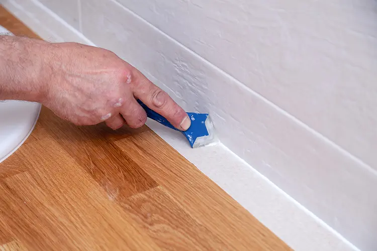 Man using a sealant smoothing tool to finish off a fresh bead of white silicone sealant