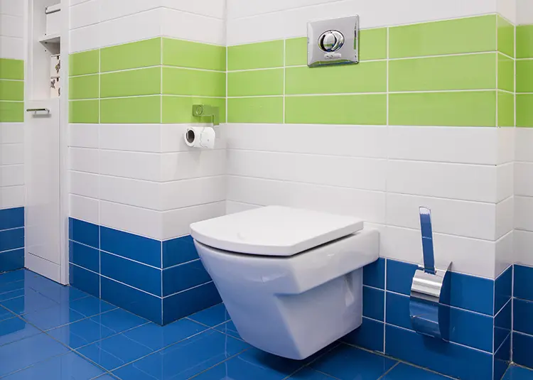 A wall-mounted toilet in a bathroom with white, green, and blue tiled walls and a blue tiled floor.