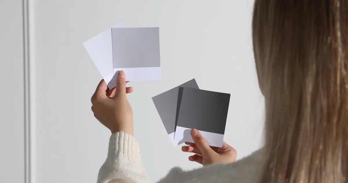 Choosing The Right Shade A woman comparing white and grey colour shades and swatches for interior design in a bright room.